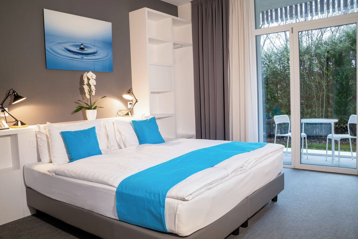 Un dormitorio moderno con una cama grande, una orquídea en maceta y vistas al exterior a través de un ventanal corredero.