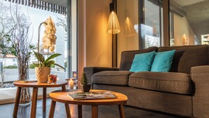 Una sala de estar moderna con un sofá marrón, dos mesitas de madera y una orquídea en maceta.