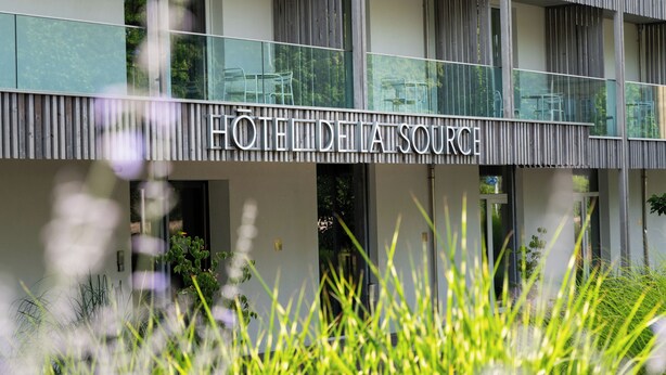 Un hotel con fachada moderna, entrada visible y un balcón con mobiliario.