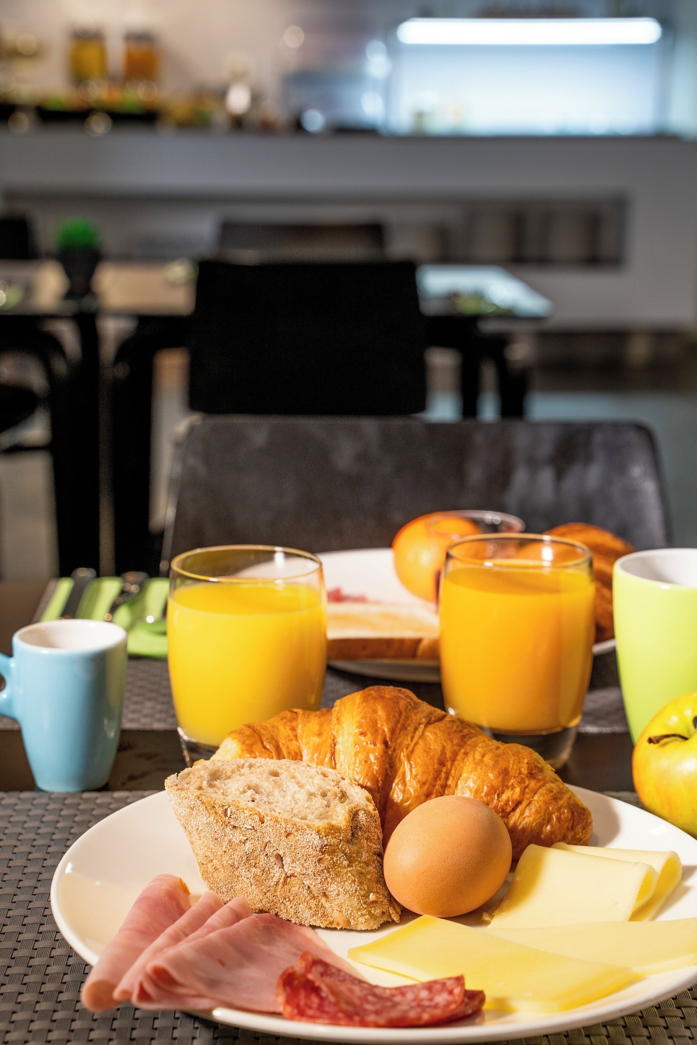 A breakfast setting with croissants, ham, cheese, an egg, and orange juice on a plate.