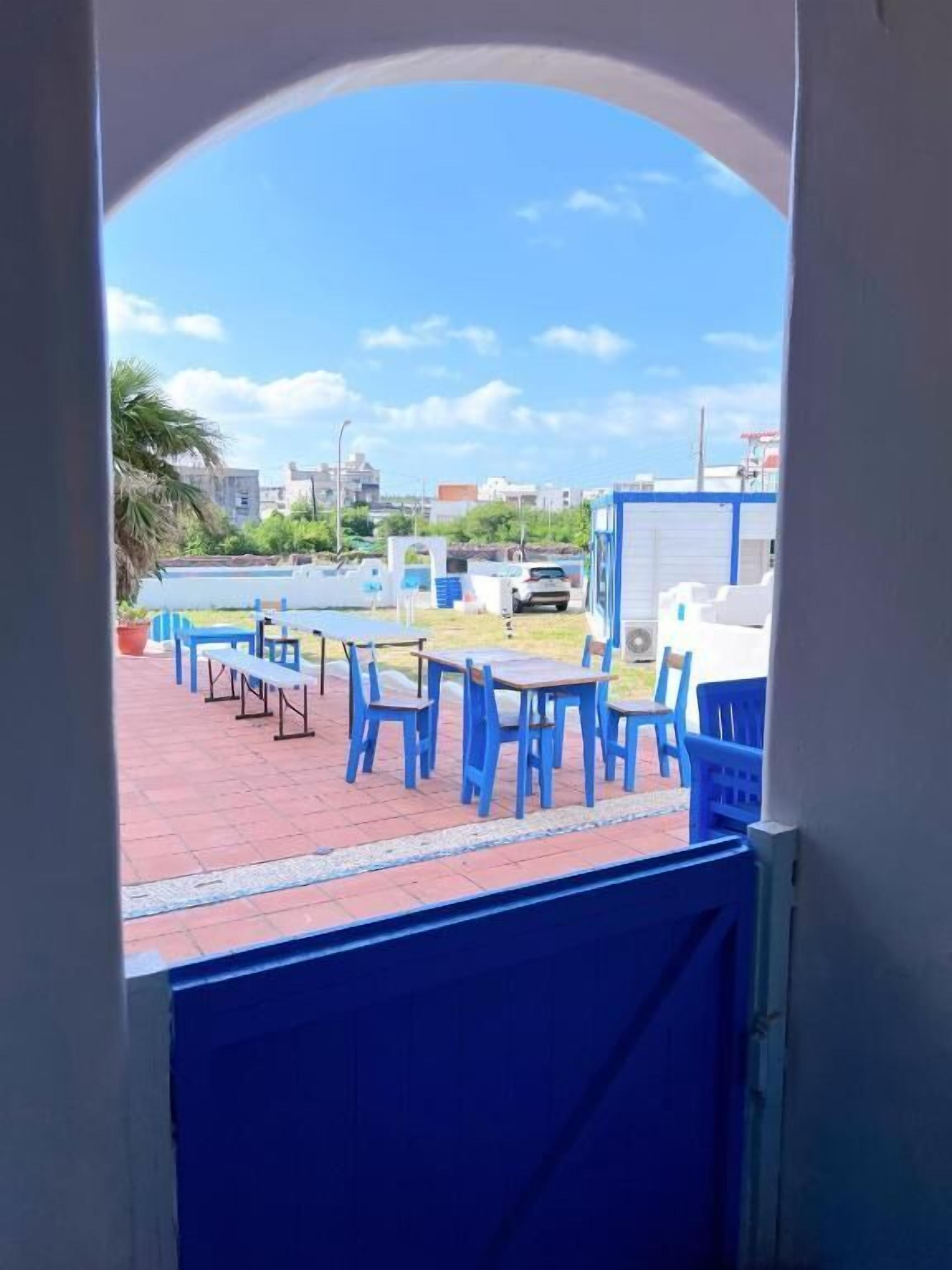 An outdoor seating area with blue tables and chairs, a paved surface, and a view of the cityscape in the background.
