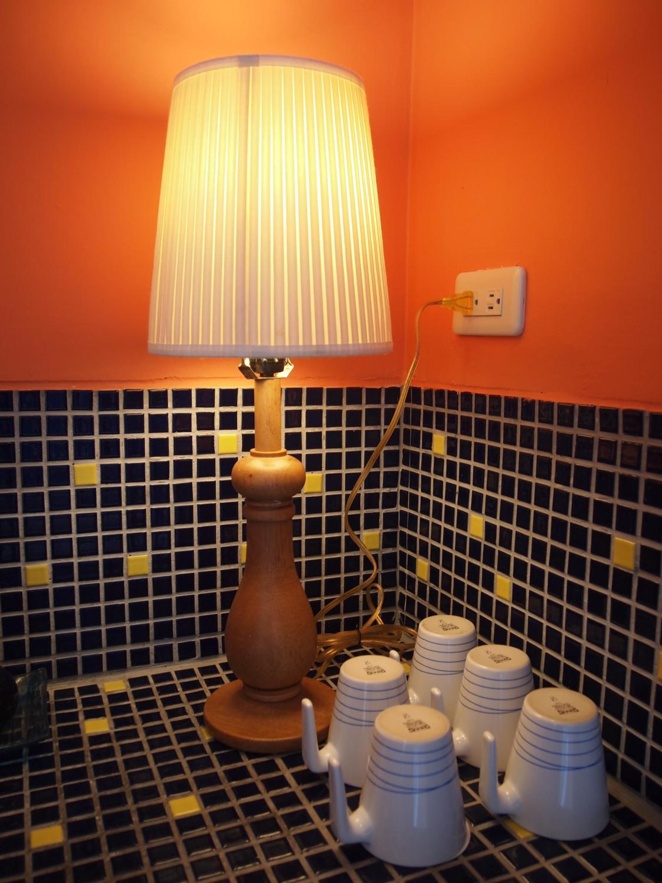 A bathroom with a wooden floor lamp, a tiled backsplash, and a set of white mugs on a tray.