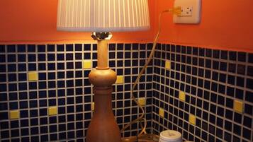 A bathroom with a wooden floor lamp, a tiled backsplash, and a set of white mugs on a tray.