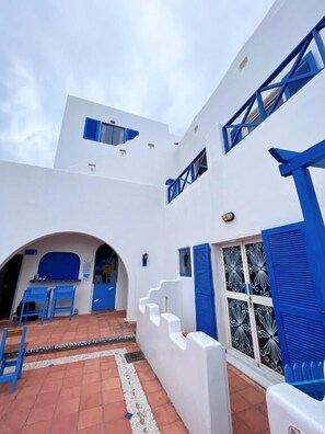 A white building with blue accents, including shutters and railings. There is a covered outdoor seating area with blue chairs. - Greek frontier villa (Magong)