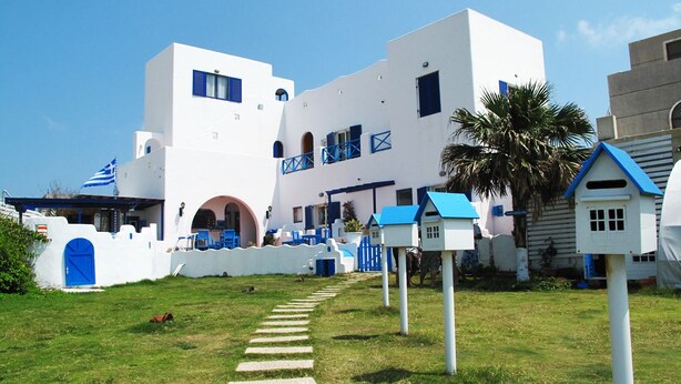 A white building with blue accents, a pathway leading to the entrance, and small blue birdhouses. - Greek frontier villa (Magong)