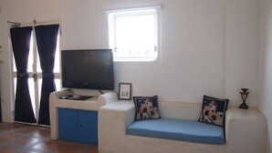 A living room with a TV, a sofa with cushions, a window, and a door with curtains. - Greek frontier villa (Magong)