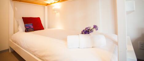 Habitación individual con una cama, techo de madera, paredes blancas y almohada roja.