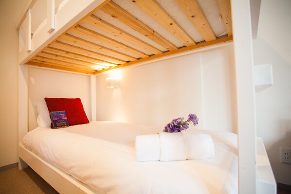 A single-bed room with a wooden ceiling, white walls, and a red pillow. - Yutaka Townhouse (Kutchan)