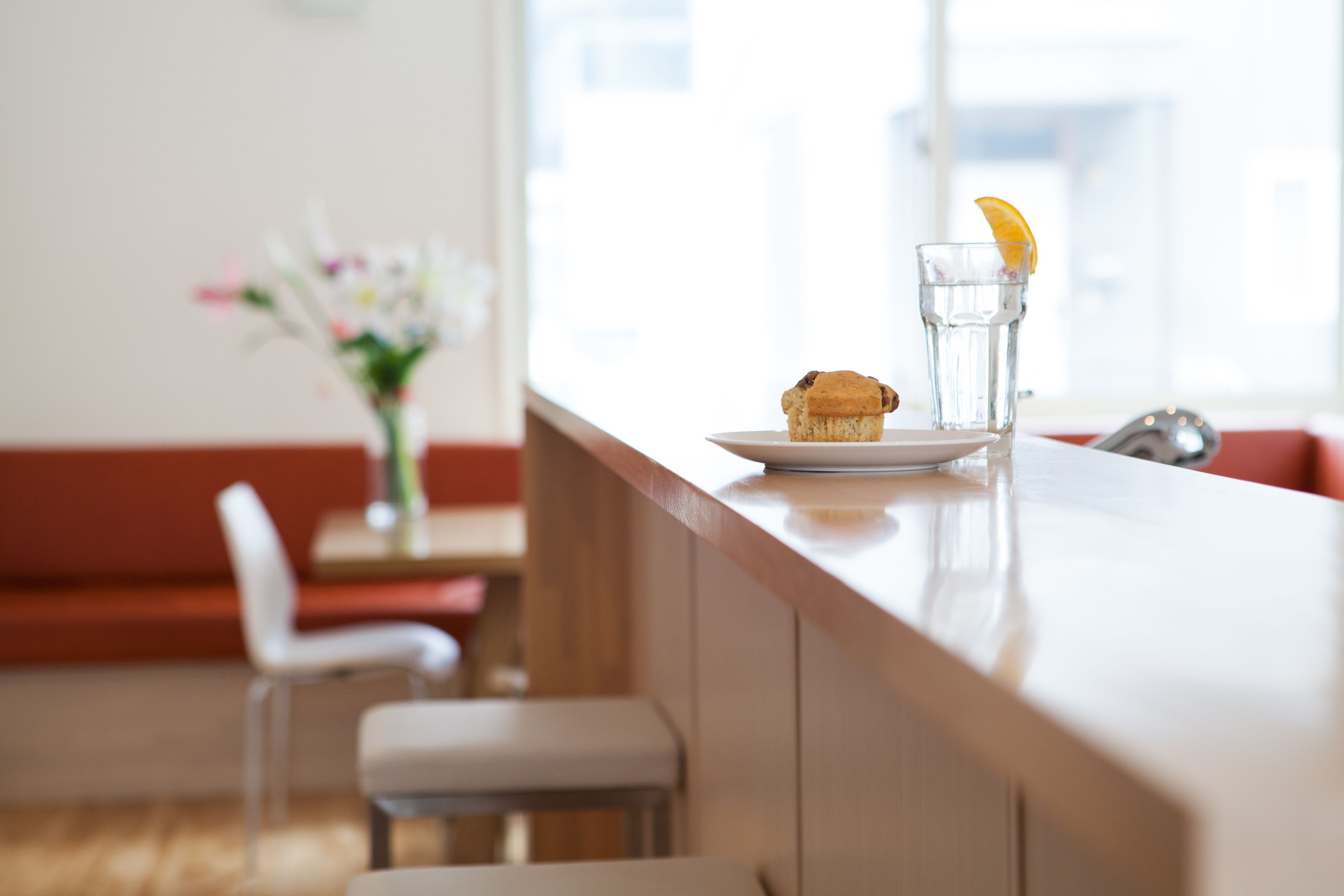 A clean, modern dining area with a wooden counter, a plate with a muffin, and a glass of water with an orange slice.