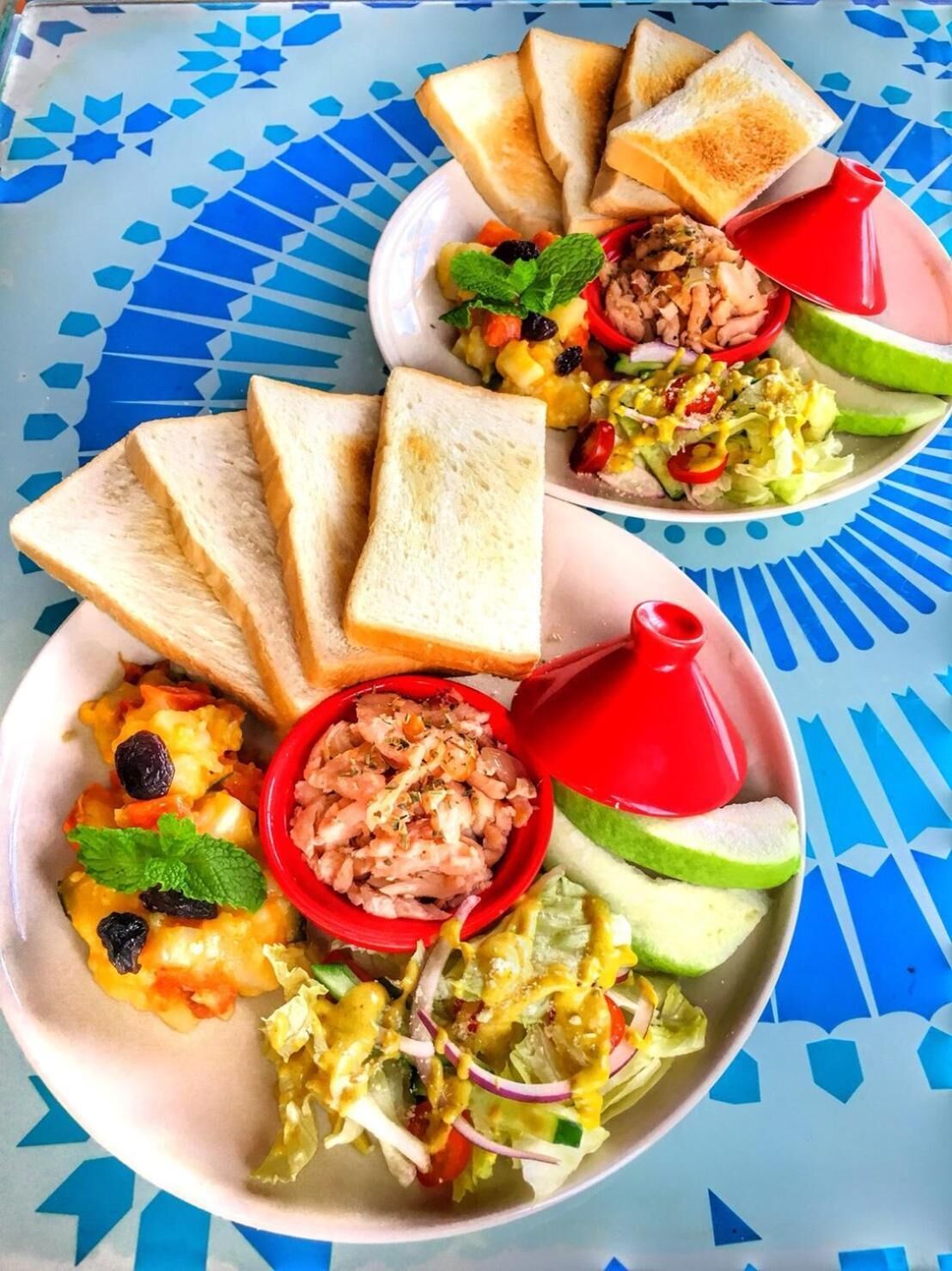 A meal with toast, a salad, and a bowl of food on a patterned tablecloth.