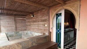 A wooden cabin interior with a stone hot tub, a small kitchen, and a decorative archway. - Raid Gardden Boutique Hotel (Magong)