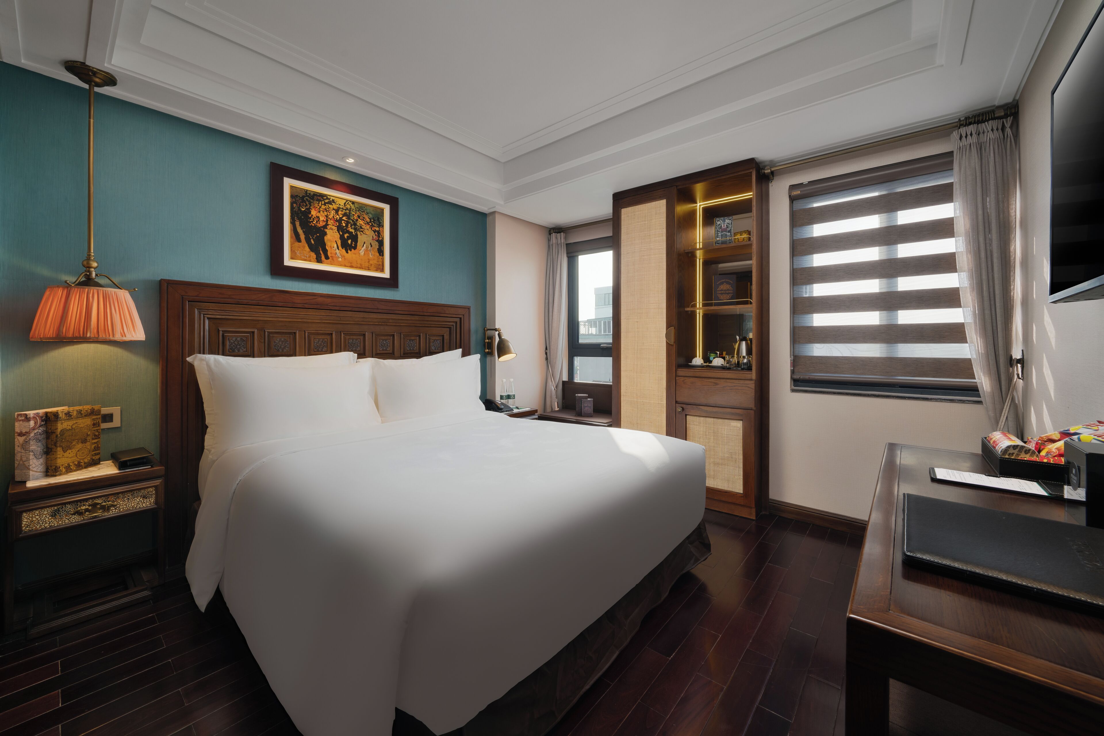 A hotel room with a large bed, a nightstand with a lamp, a television, and a window with blinds.