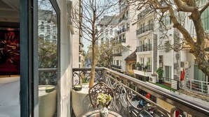 A balcony with a table, a vase with flowers, and a view of the street below. -  Peridot Gallery Classic Hotel (Hanoi)
