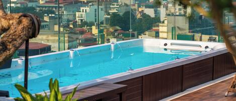 Une piscine sur le toit offrant une vue sur la ville, avec une terrasse en bois et des espaces de détente.