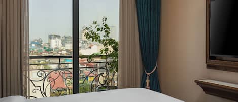 Habitación de hotel con una ventana grande, una cama, un televisor y vistas a la ciudad.