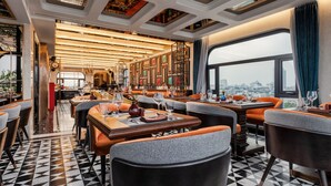 A restaurant with a modern interior, featuring a black and white tiled floor, orange and grey upholstered chairs, and a city view through large windows. -  Peridot Gallery Classic Hotel (Hanoi)