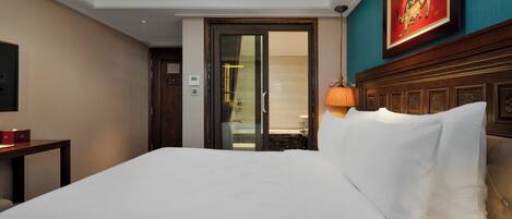 A hotel room with a large bed, a wooden headboard, a painting on the wall, and a door leading to a bathroom.