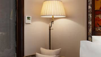 A hotel room with a bed, a bedside lamp, a thermostat, and a window with a curtain.