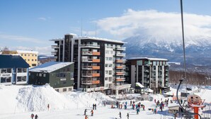 A modern ski resort with multi-story buildings, a ski lift, and a snowy mountain backdrop.