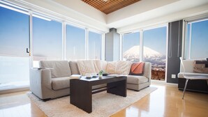 A modern living room with a large sofa, a coffee table, and a view of a mountain through large windows.