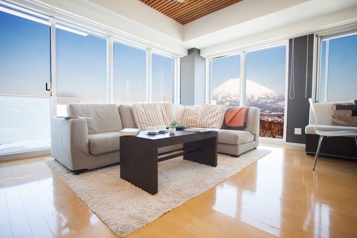 A modern living room with a large sofa, a coffee table, and a view of a mountain through large windows.