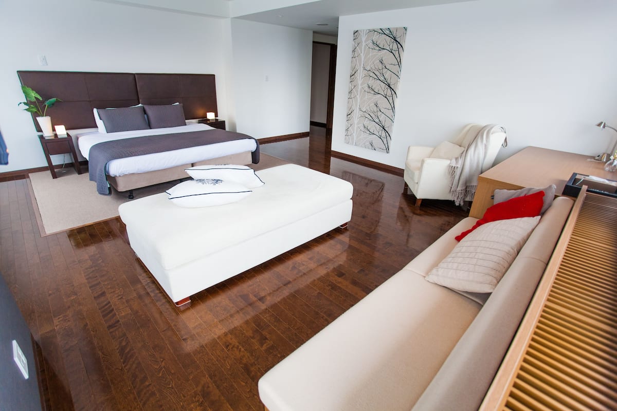 A modern hotel room with a large bed, a sofa, a desk, and a chair.