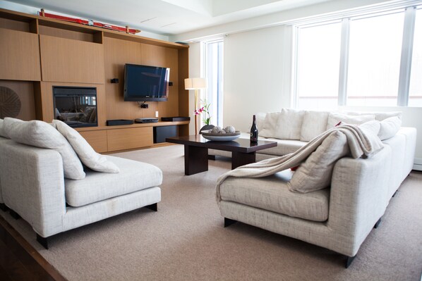 A modern living room with two sofas, a coffee table, a flat-screen TV, and a fireplace.