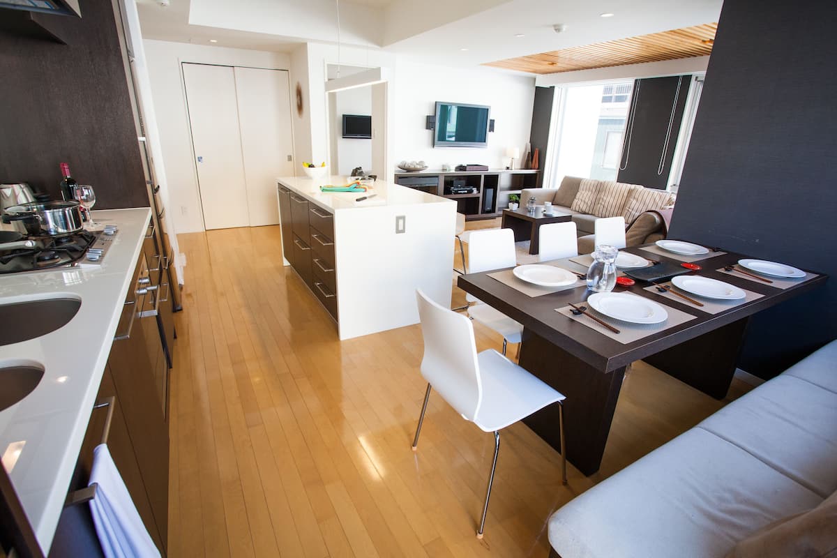 A modern kitchen with a dining area, wooden flooring, and a large window.