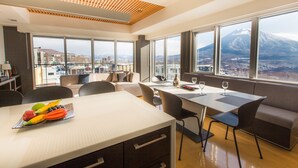 A modern hotel room with a large dining table, comfortable seating, and a view of a mountain.