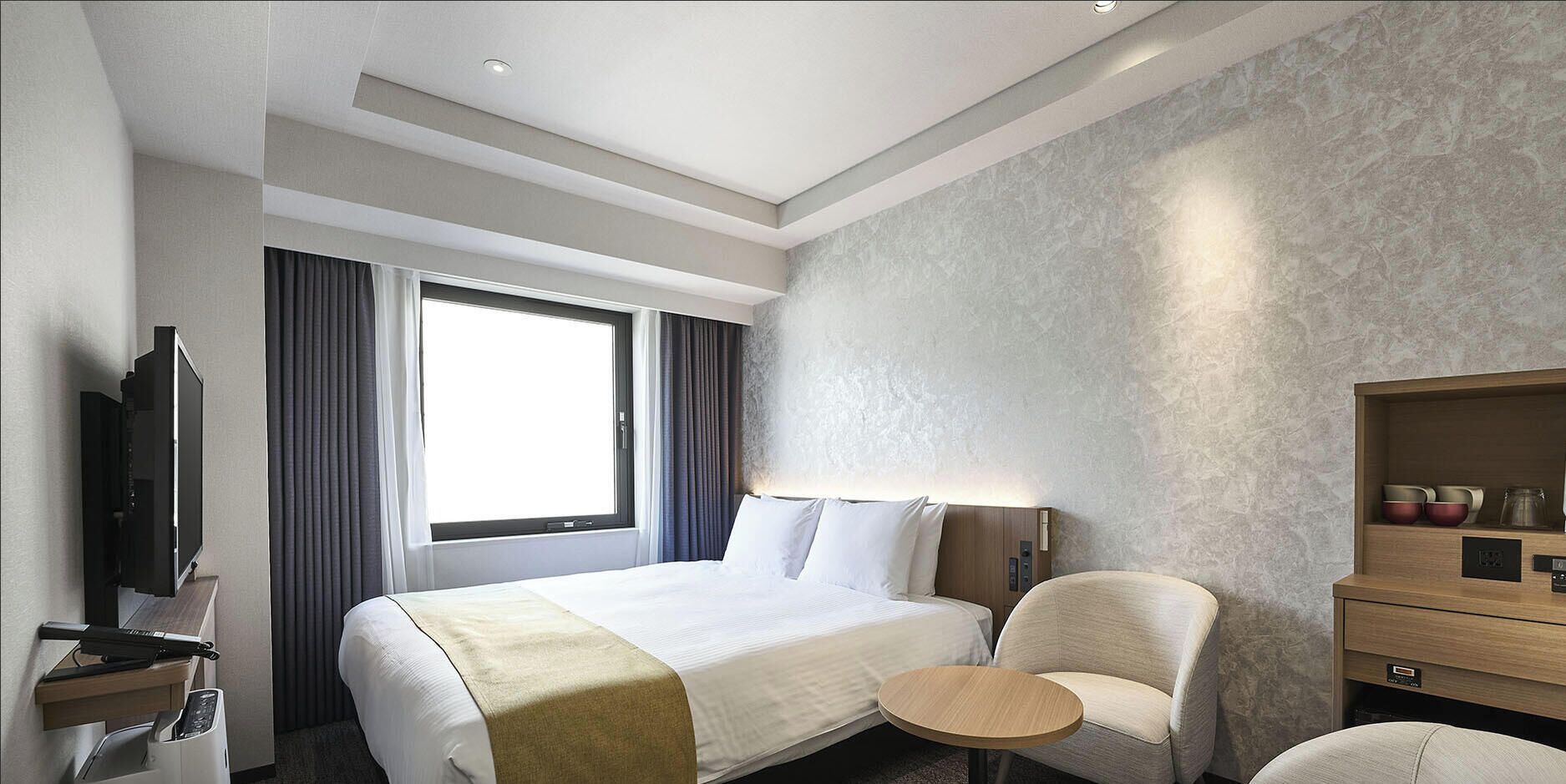 Une chambre d’hôtel comprenant un lit, une télévision, une chaise, une petite table et un meuble en bois.