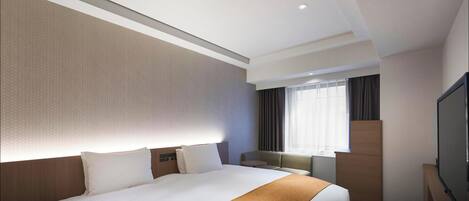 Ein Hotelzimmer mit einem großen Bett, einem Flachbildfernseher, einem Fenster mit Vorhängen und einem kleinen Tisch.