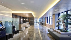 Un moderno vestíbulo de hotel con un mostrador de recepción alargado, áreas de descanso y un amplio ventanal con vistas al exterior.