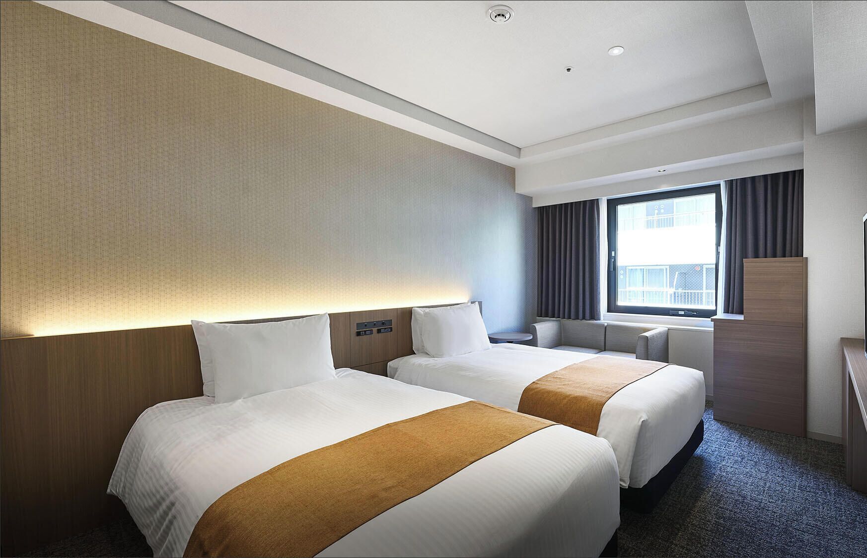 Une chambre d’hôtel avec deux lits, un bureau, une chaise, une fenêtre avec des rideaux et un panneau de commande fixé au mur.