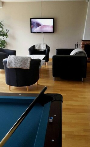 A pool table in a room with two black armchairs and a television mounted on the wall. - Kosta Lodge (Kosta)
