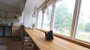 Una cocina con mostradores de madera, un comedor con sillas y un ventanal con vistas a árboles y una casa.