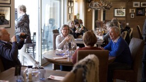 Un grupo de personas sentadas alrededor de una mesa redonda en un restaurante con vistas a la ciudad a través de amplias ventanas.