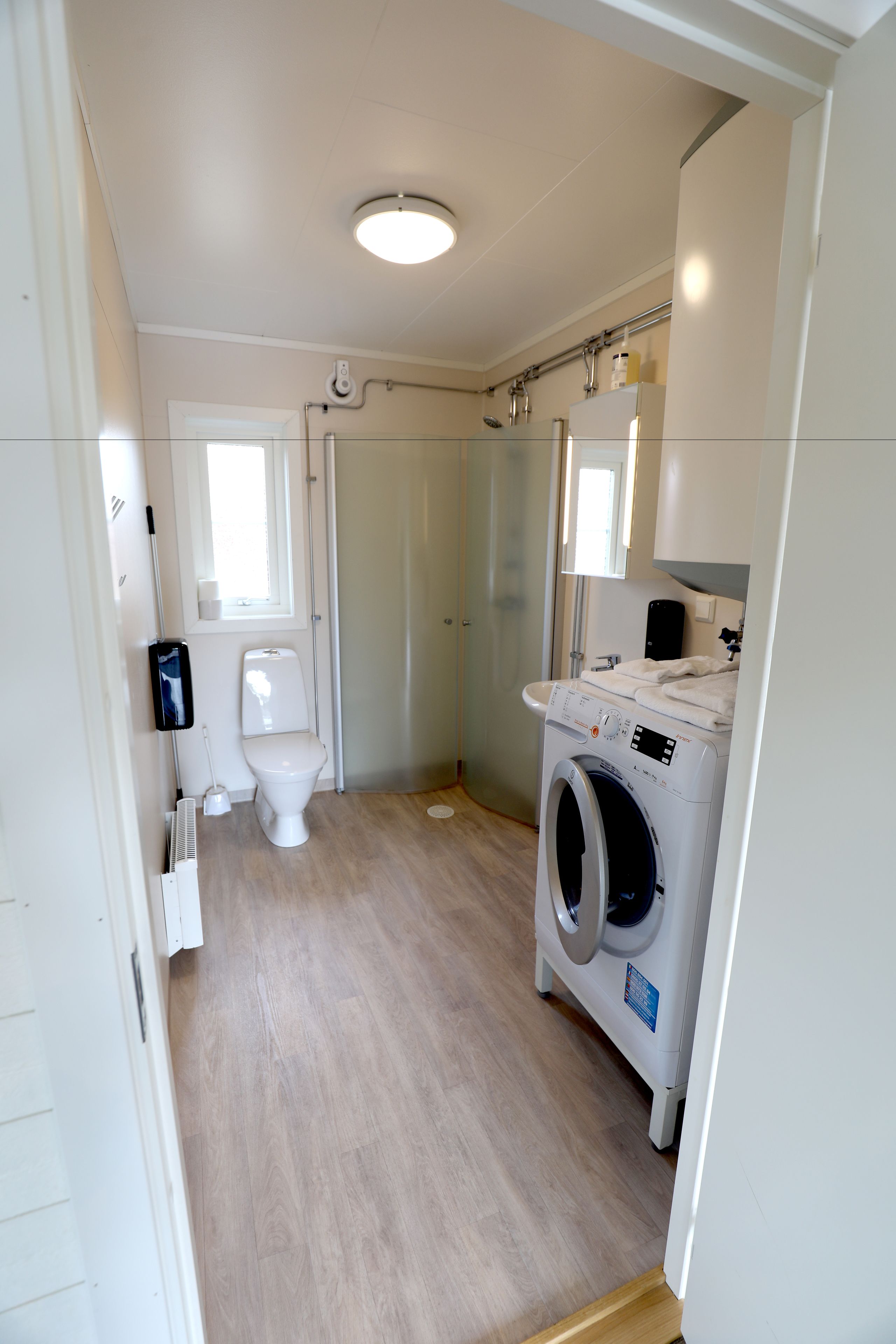 A compact bathroom with a toilet, washing machine, and a window.