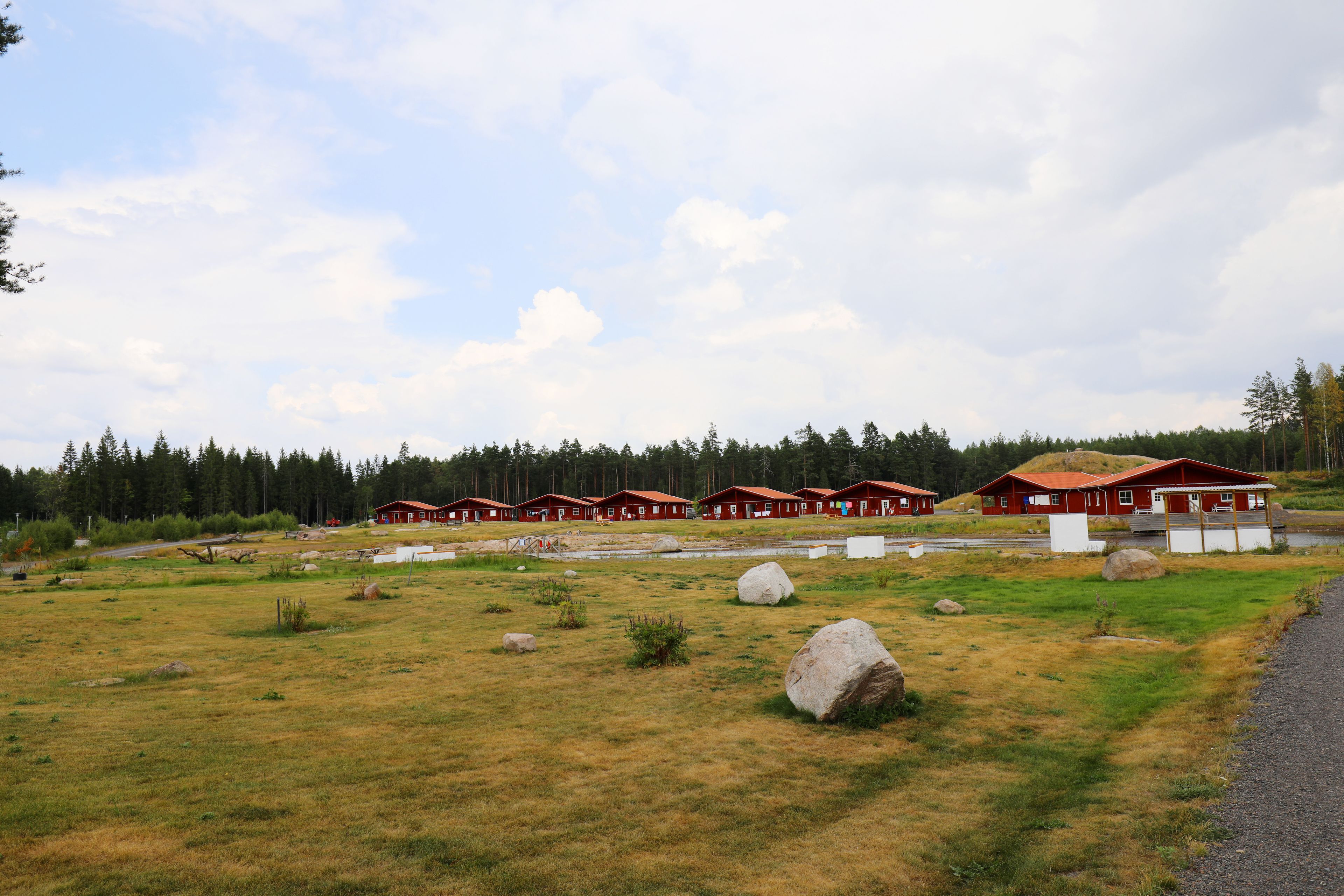 Fileira de cabanas vermelhas com um campo gramado e uma floresta ao fundo.