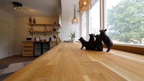 Una mesa de madera para comer con tres figuras de animales negros, una planta y un estante con varios objetos.