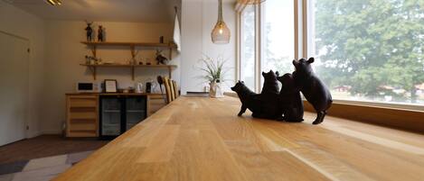 Una mesa de madera para comer con tres figuras de animales negros, una planta y un estante con varios objetos.
