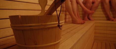 Un balde de madera con asa sobre un piso de madera, probablemente en una sauna o baño de vapor.