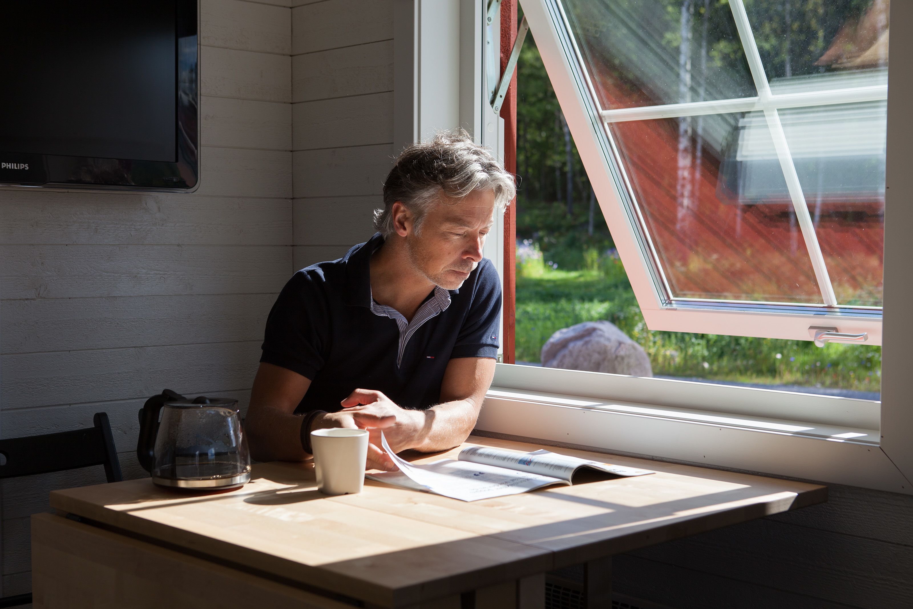 A man sitting at a table by a window with a view of greenery outside.