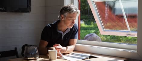 A man sitting at a table by a window with a view of greenery outside.