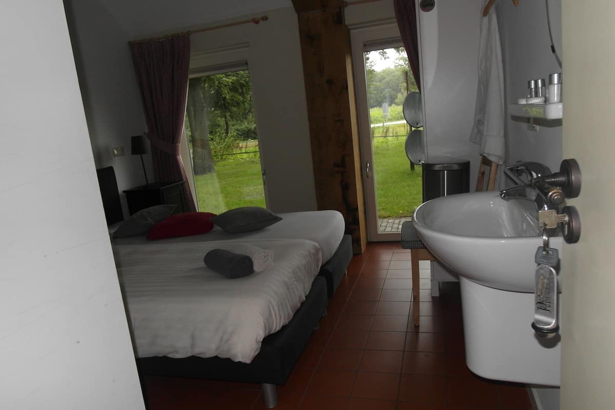 Ein Schlafzimmer mit Bett, Nachttisch, einem Fenster mit Vorhängen und Blick ins Freie.