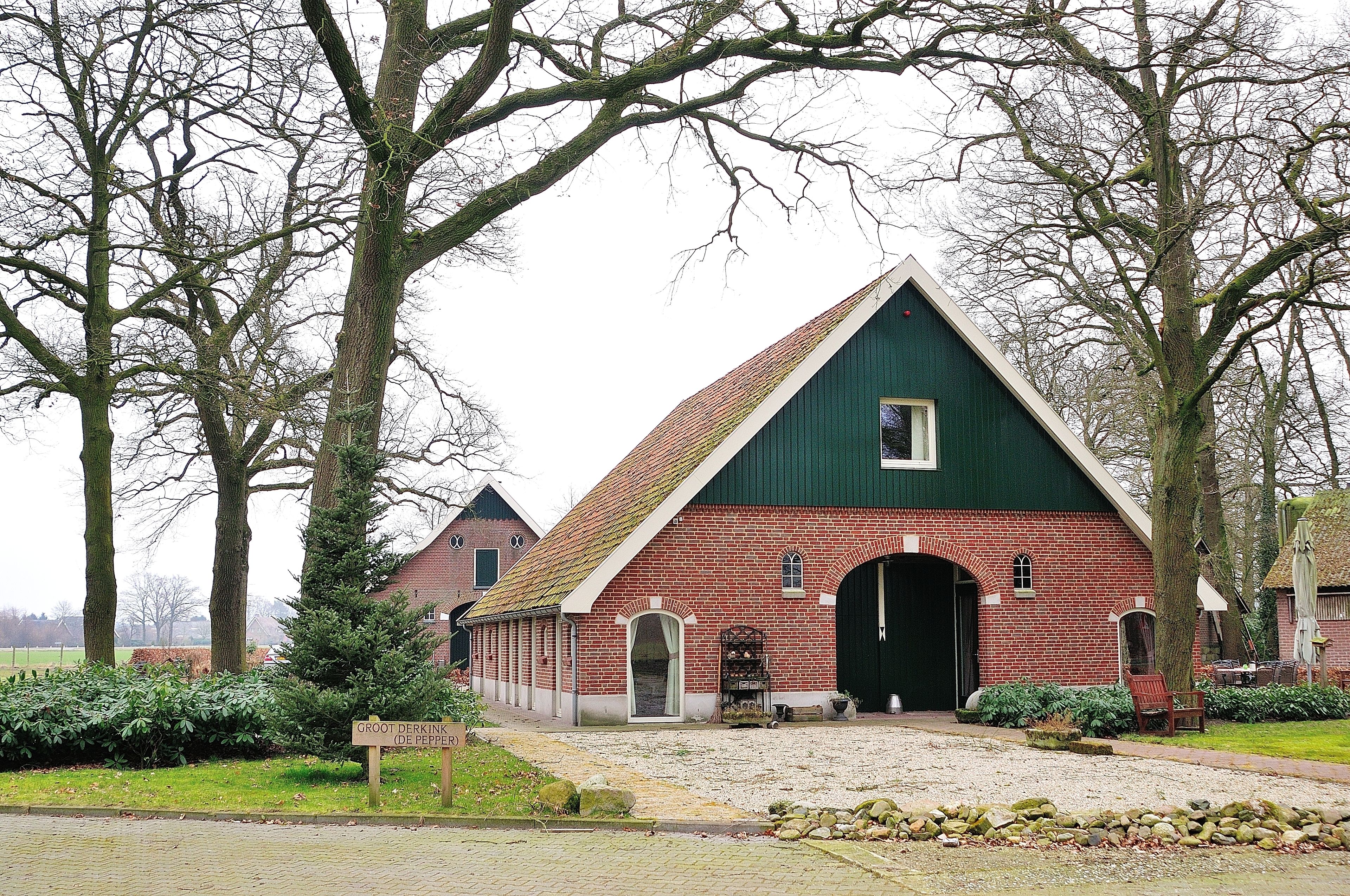 A traditional brick building with a green roof and arched entrance, surrounded by trees and a gravel path.