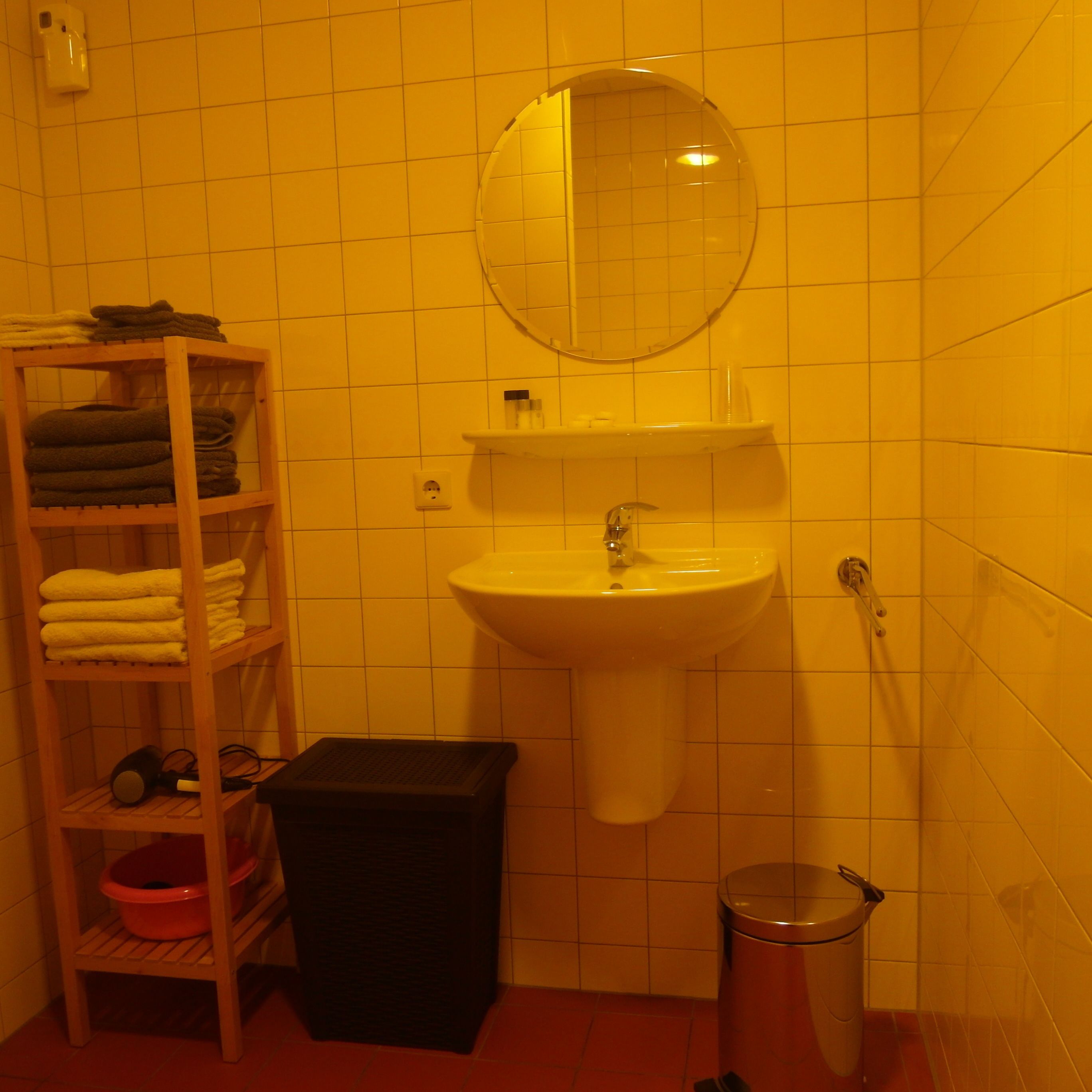 Une salle de bain équipée d’un lavabo, d’un miroir, d’une étagère avec des serviettes et d’une poubelle.