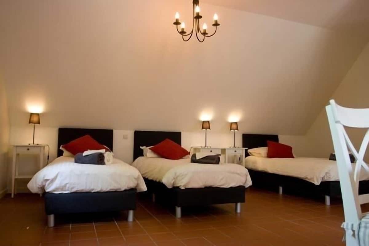 Ein Zimmer mit drei nebeneinander stehenden Betten, jeweils mit Nachttisch und Lampe.