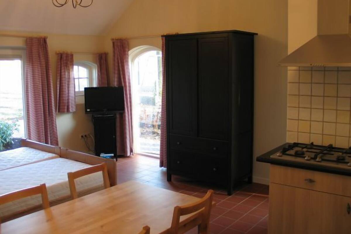 Eine Küche mit Esstisch, Stühlen, einem schwarzen Schrank, einem Fernseher und einem Gasherd.