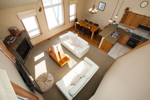 A spacious living area with a white sofa, a dining table, and a kitchen with wooden cabinets and a built-in oven. - Niseko Alpine Apartments (Kutchan)