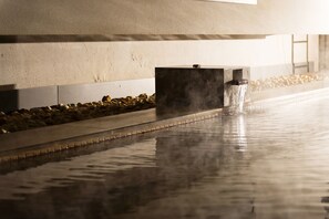 A water feature with a stream flowing into a reflective pool, surrounded by a pebble bed and a concrete structure.